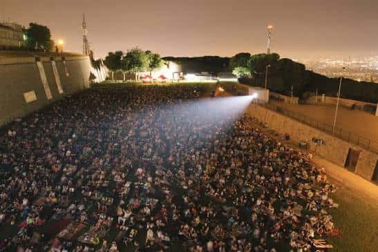 Escena nocturna del cine al aire libre con proyección y multitud bajo las luces