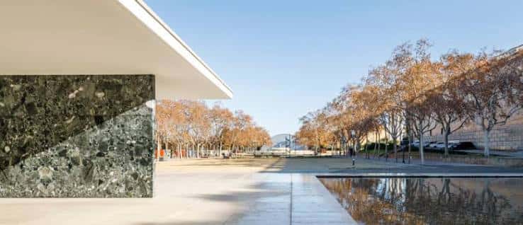 Detalle arquitectónico del muro de travertino y columna de acero con árboles al fondo