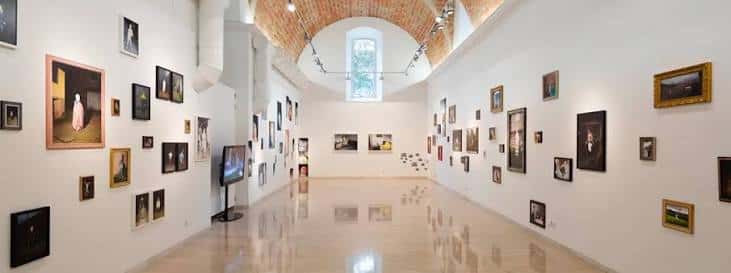 Interior de la sala de exposiciones con bóvedas de ladrillo y obras colgadas en las paredes