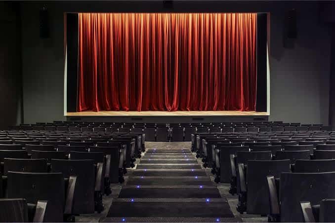 Escenario del Teatro Goya con cortinas rojas cerradas y butacas vacías frente a él