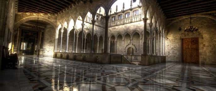 Vista del claustro gótico con arcos apuntados y suelo de mármol geométrico