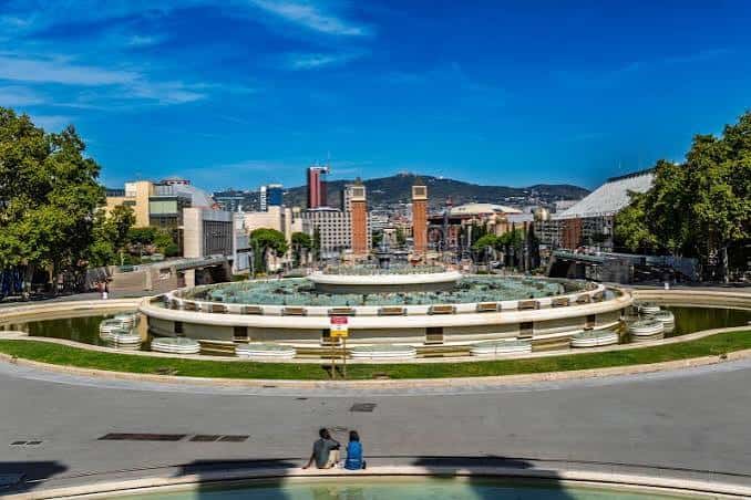 Plaza de la Font del Mont en día soleado, con la fuente en el centro y personas descansando en primer plano