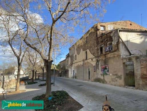 Vista de la calle Carrer d'Alarcón con edificios de piedra y árboles sin hojas bajo un cielo azul