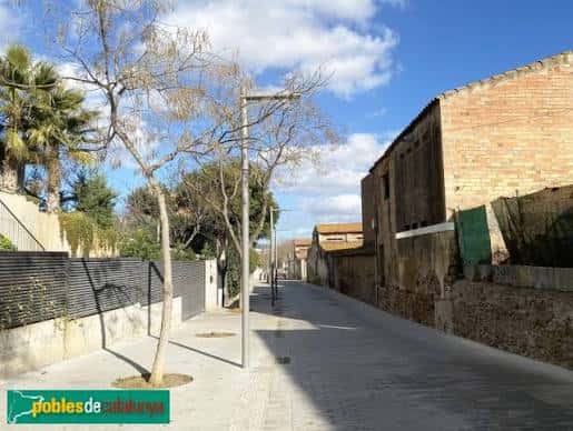 Calle Carrer d'Alarcón con árboles jóvenes, farolas y muros de piedra bajo el sol