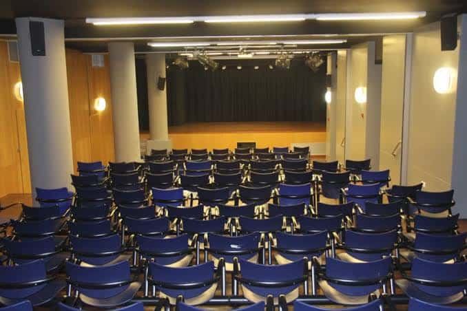 Interior del teatro con butacas azules y escenario iluminado