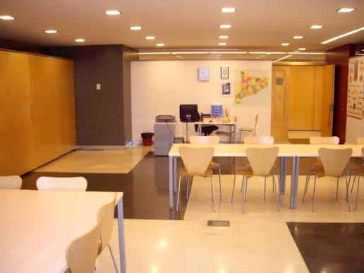 Sala interior del centro con mesas y sillas dispuestas para reuniones o talleres