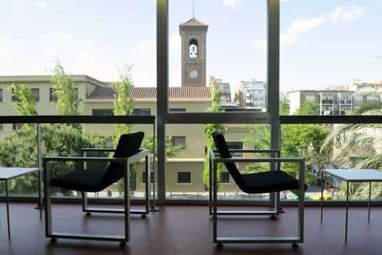 Interior de la biblioteca con vistas a la ciudad y zona de lectura junto a ventanales