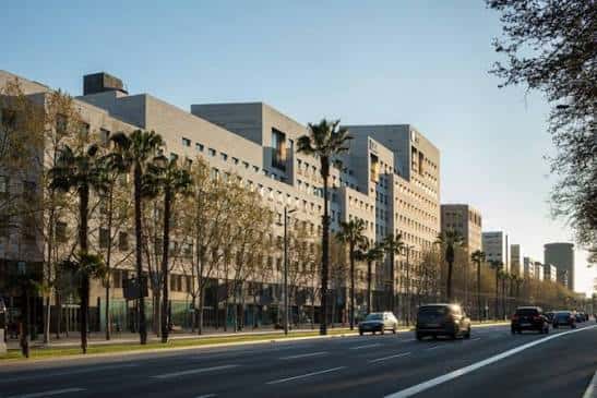 Perspectiva lateral del edificio L'Illa Diagonal desde la avenida, con tráfico y árboles alineados