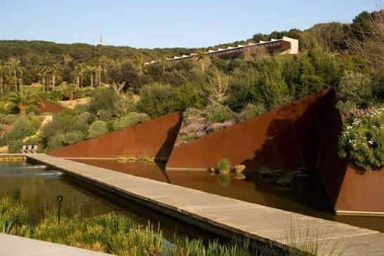 Estructura arquitectónica de acero oxidado junto a un canal de agua en el jardín