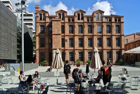 Fachada principal del edificio de la UPF con estudiantes en el patio exterior bajo toldos