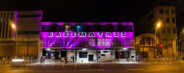Fachada frontal de la Sala Razzmatazz iluminada en morado durante la noche
