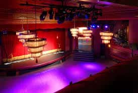 Vista del escenario vacío con cortinas rojas y luces de escenario