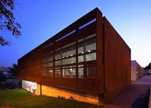 Fachada nocturna de la biblioteca con revestimiento de madera oscura y ventanas iluminadas
