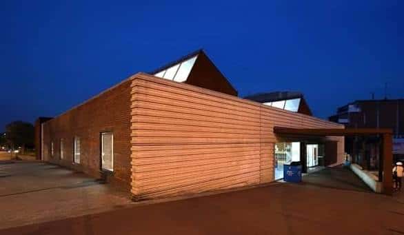 Ángulo exterior de la biblioteca al atardecer, mostrando la textura de madera y la entrada principal