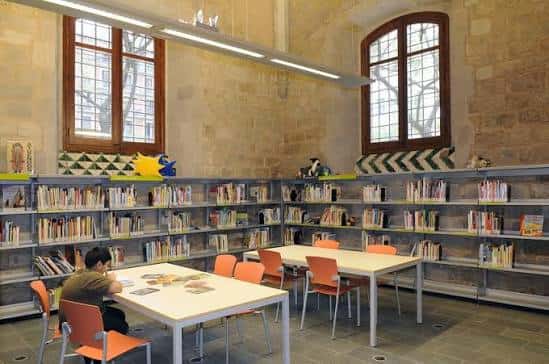 Sala infantil de la biblioteca con mesas, sillas naranjas y estanterías bajas