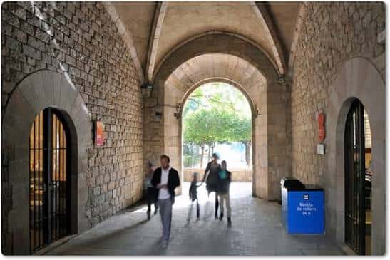 Pasillo con arcos de piedra y gente caminando hacia el exterior