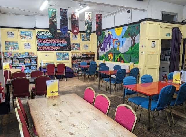 Sala de juegos con mesas y sillas, decorada con murales coloridos y banderines temáticos