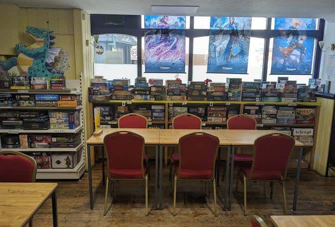 Área de juegos con estanterías llenas de juegos de mesa y mesas preparadas para eventos