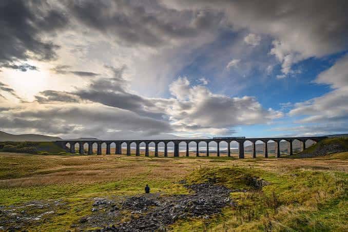 Vista panorámica del viaducto de Ribblehead con el tren cruzando bajo un cielo dramático