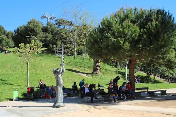 Vista del parque con la escultura de la mujer sosteniendo una silla y personas descansando en bancos