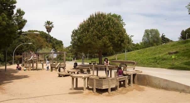 Área de juegos infantiles con estructuras de madera y árboles en los Jardines de Joan Brossa