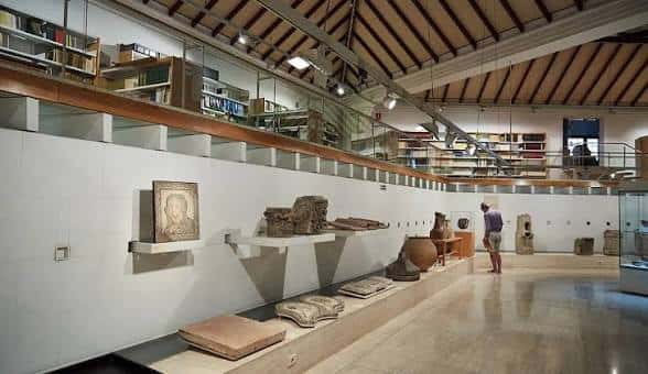 Galería interior con artefactos expuestos en estanterías blancas y techo de vigas de madera