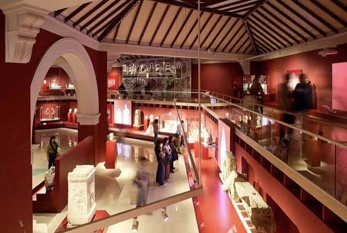 Vista panorámica del interior del museo con paredes rojas, múltiples niveles y visitantes recorriendo las exposiciones
