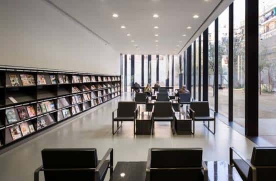 Interior de la biblioteca con estanterías, zonas de lectura y grandes ventanales