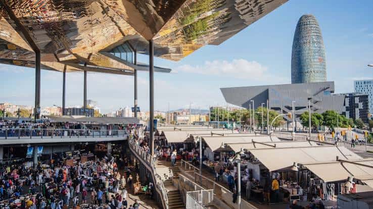 Vista panorámica del interior del Mercat dels Encants con su distintiva cubierta reflectante y la Torre Glòries al fondo