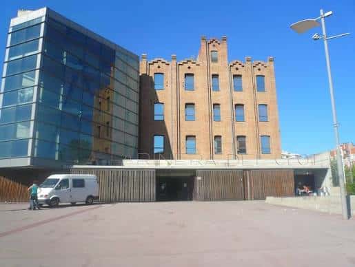 Vista exterior del Centre Cultural La Farinera del Clot mostrando la fachada histórica de ladrillo junto a la ampliación moderna de cristal