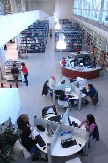 Interior de la biblioteca mostrando el área de lectura con mesas, ordenadores y estanterías de libros