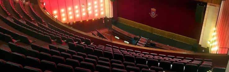 Interior del auditorio con butacas rojas, escenario iluminado y cortina frontal decorada