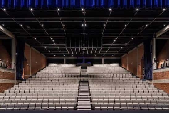 Interior del auditorio con butacas blancas dispuestas en gradas y escenario con cortinas azules