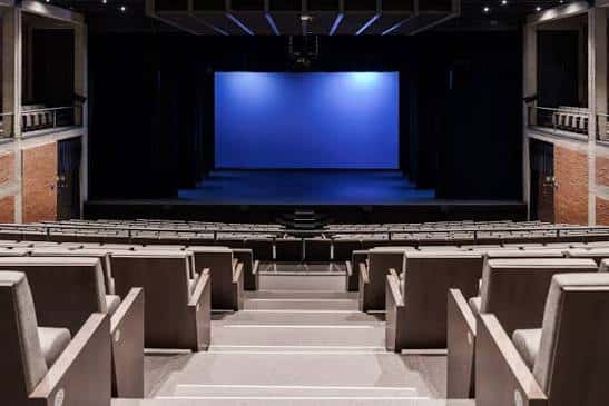 Vista frontal del escenario con pantalla azul y butacas grises en el auditorio