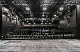 Interior del auditorio principal con butacas negras y escenario amplio bajo iluminación profesional