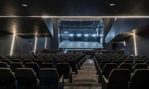 Vista desde la platea hacia el escenario con diseño arquitectónico contemporáneo y luces de acento