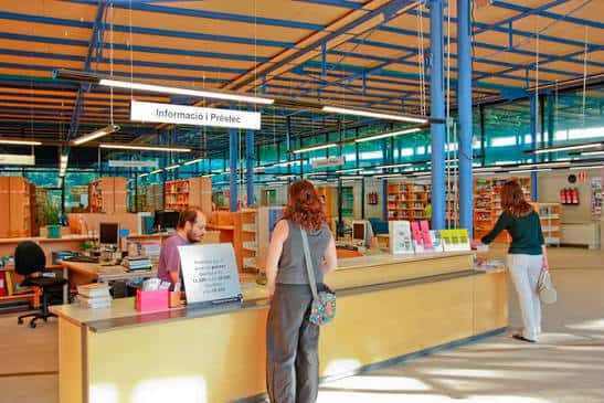 Interior de la biblioteca mostrando el mostrador de información y préstamo con usuarios