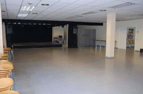 Sala polivalente con escenario y sillas apiladas, ideal para eventos