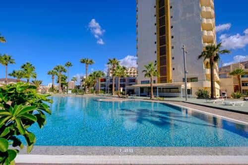 Vista de la piscina principal del complejo con el edificio de apartamentos al fondo
