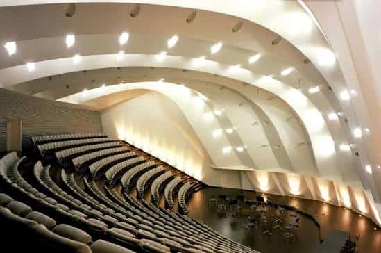 Interior del auditorio mostrando las butacas curvas y el techo ondulado con iluminación cálida