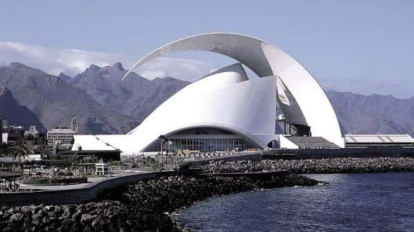 Vista diurna del Auditorio de Tenerife con montañas al fondo y acceso peatonal junto al agua