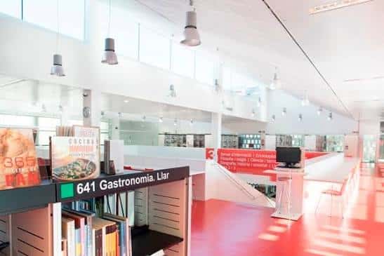 Sección de la biblioteca con estanterías de gastronomía, zona de lectura y suelo rojo característico