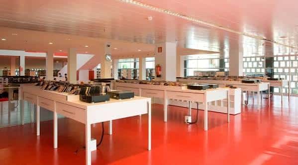 Zona de lectura y trabajo con mesas blancas y suelo rojo brillante en el interior de la biblioteca
