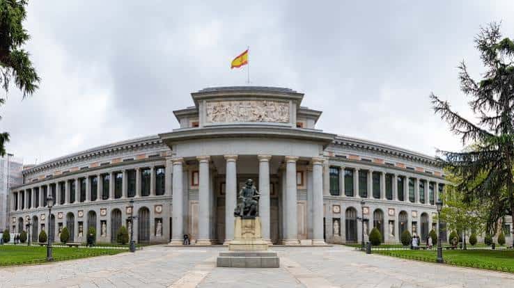 Exterior del Museo del Prado con bandera española y árboles laterales