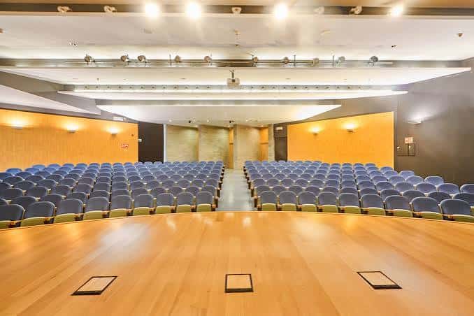 Vista general del auditorio vacío con butacas azules y escenario de madera
