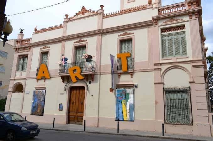 Fachada del Can Castells con letras 'ART' y obras expuestas, destacando su función como centro cultural