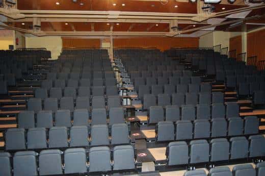 Sala de eventos con butacas grises dispuestas en gradas y techo con iluminación integrada