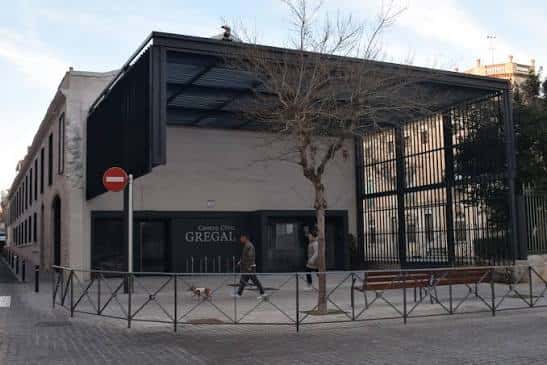 Fachada del centro cívico con personas caminando y árbol en primer plano
