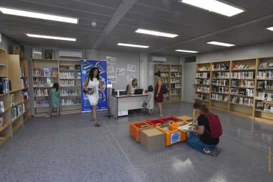 Interior de la biblioteca mostrando estanterías de libros y usuarios en la zona de préstamo