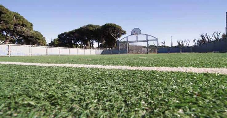 Campo de fútbol con césped artificial y aros de baloncesto al fondo